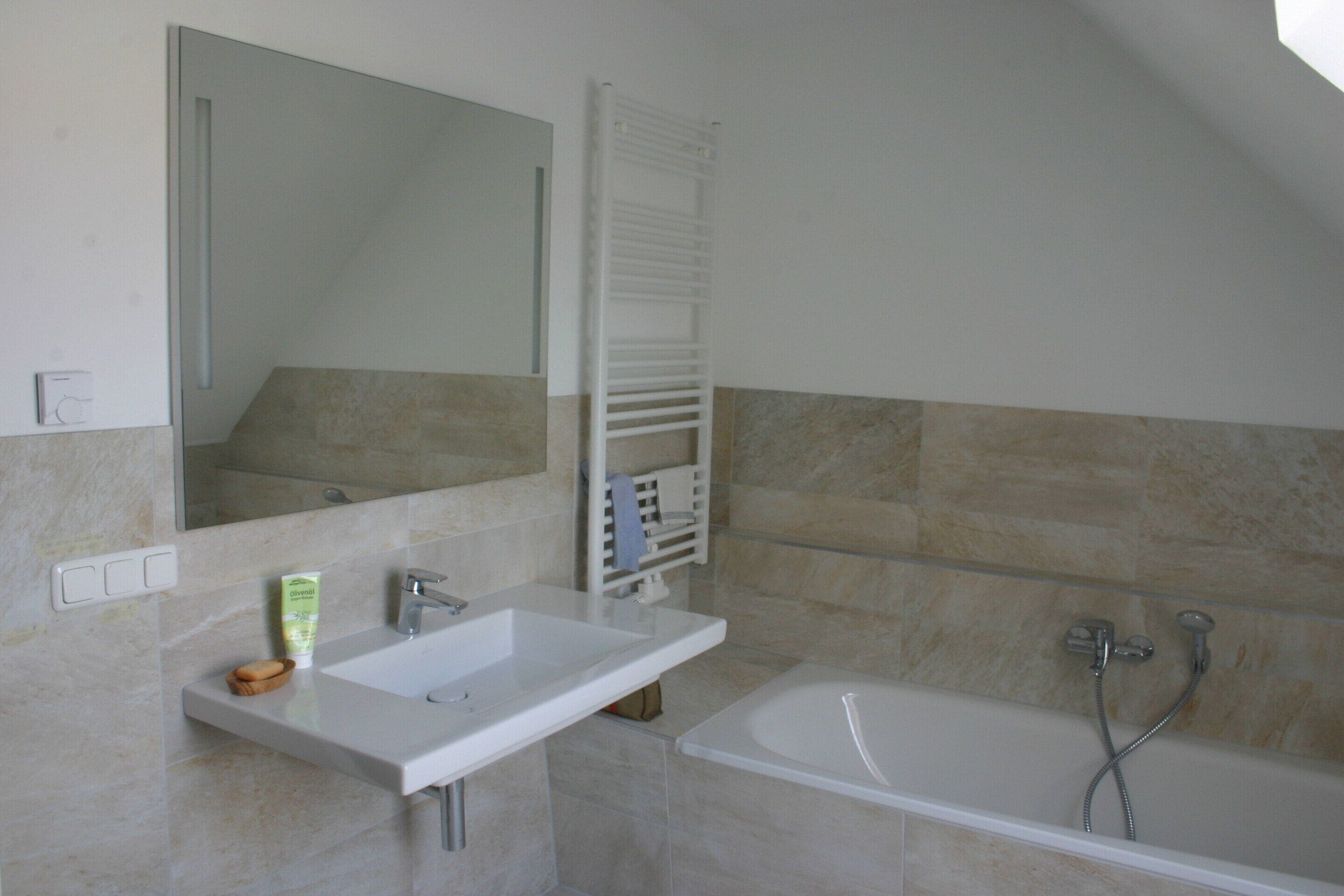 A bathroom with a sink, mirror, towel rack, and bathtub.