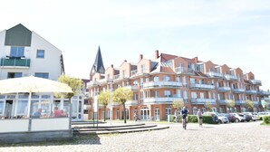 Ein mehrstöckiges Gebäude mit einem markanten Turm, ein Café mit Außenbereich und ein Parkplatz mit Fahrrädern.