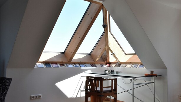 Ein Zimmer mit schrägem Dach, Oberlicht und einem Schreibtisch mit Stuhl.