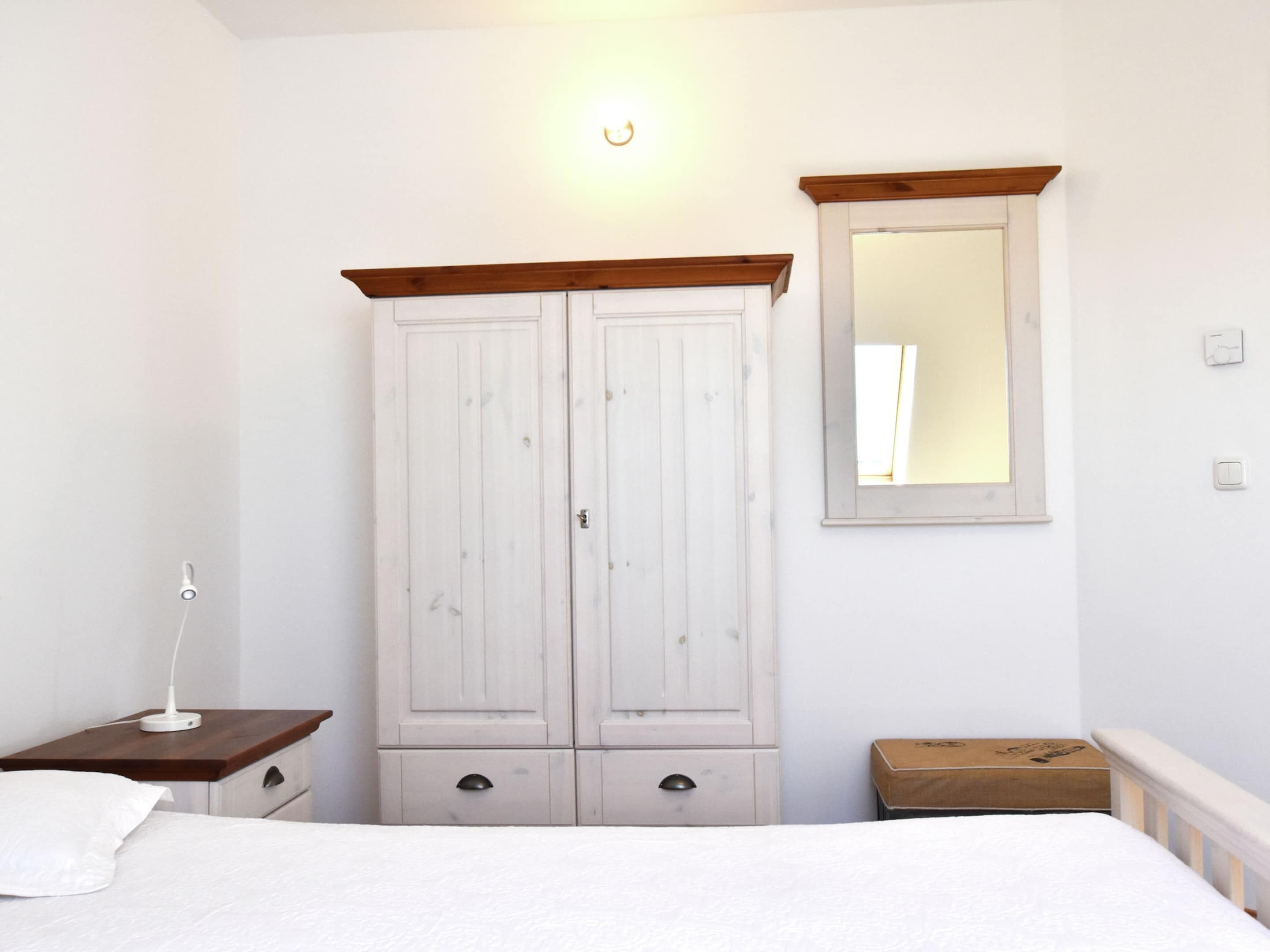 A bedroom with a bed, a wardrobe, a bedside table, a mirror, and a small box.