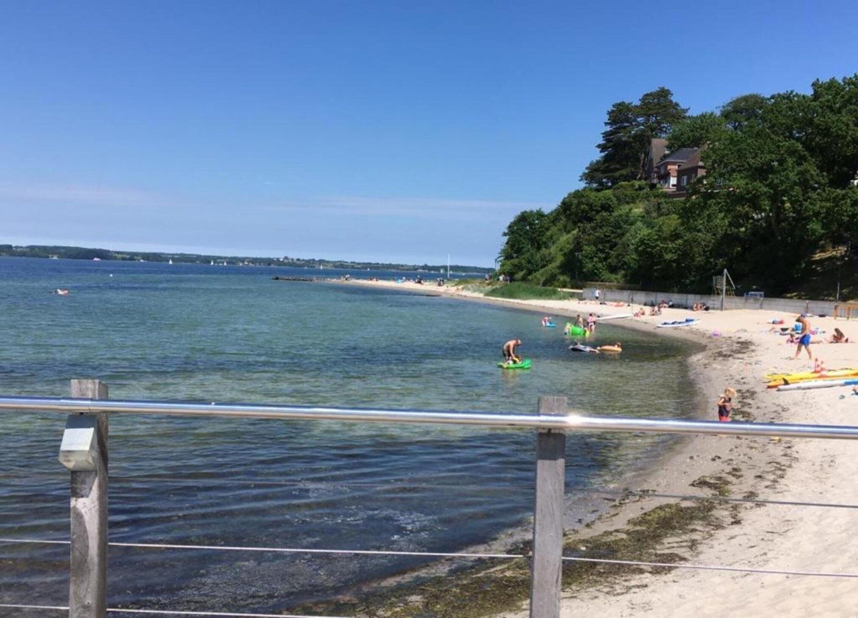 Een strand met helder water, een zandstrand en een houten hek.