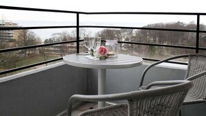 A balcony with a round table and wicker chairs, overlooking a cityscape.