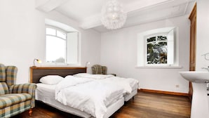 Une chambre avec un grand lit, une chaise, une table de chevet, un luminaire suspendu, une fenêtre donnant sur des arbres et un lavabo.