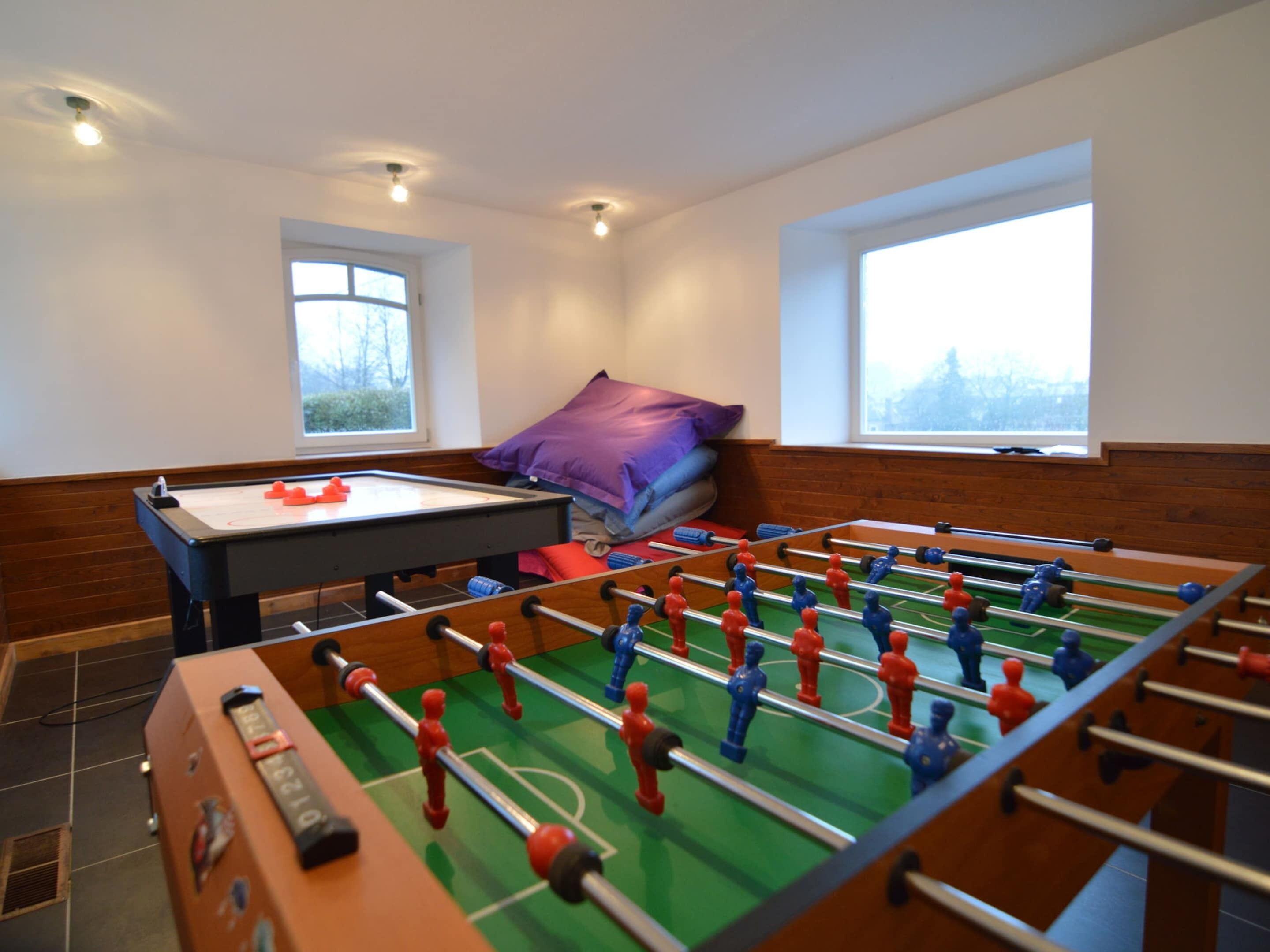 A room with two foosball tables, a pool table, and a window with a view of trees.