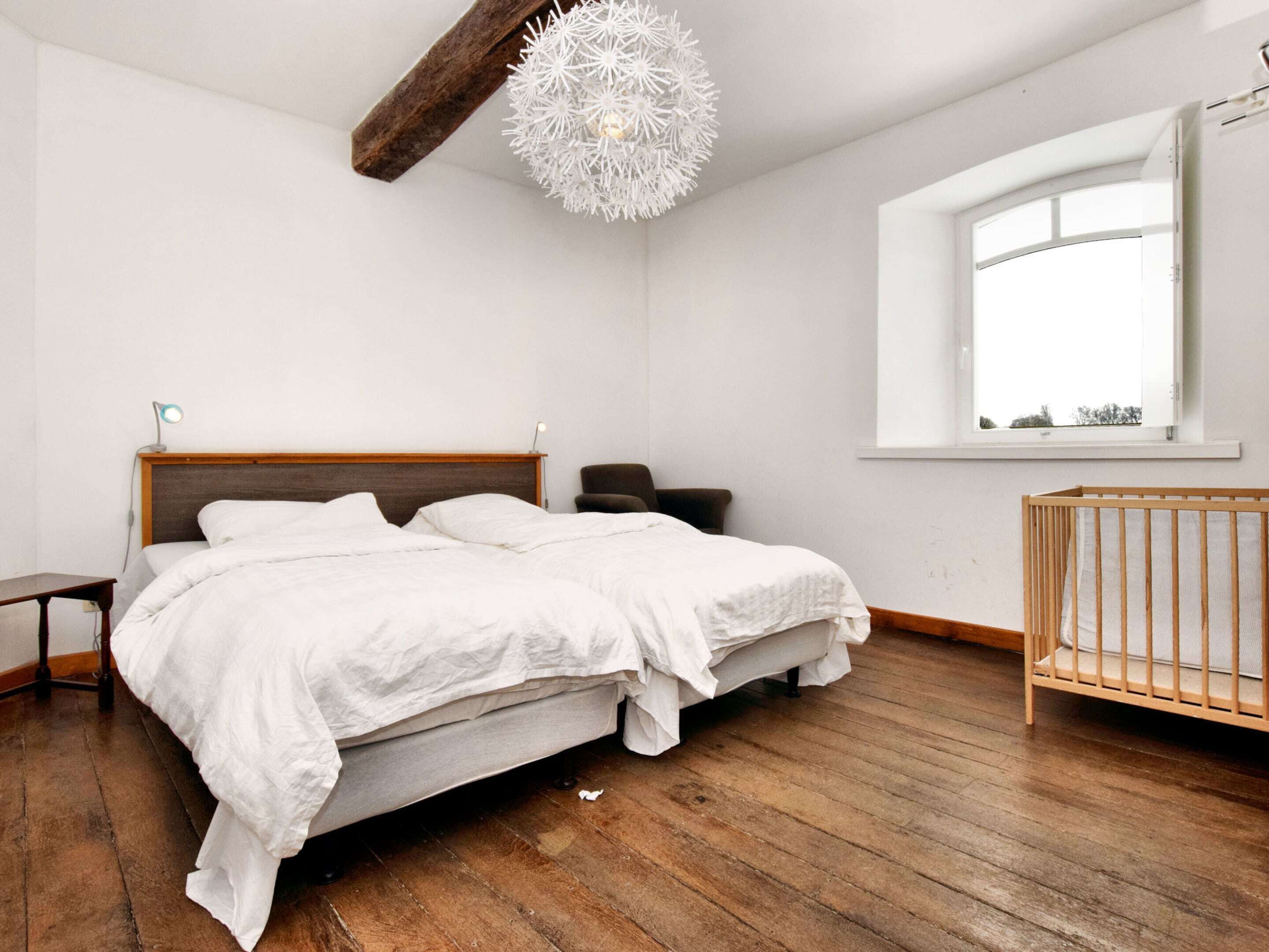 Quarto com cama de madeira, berço de madeira, escrivaninha, cadeira e uma janela grande.