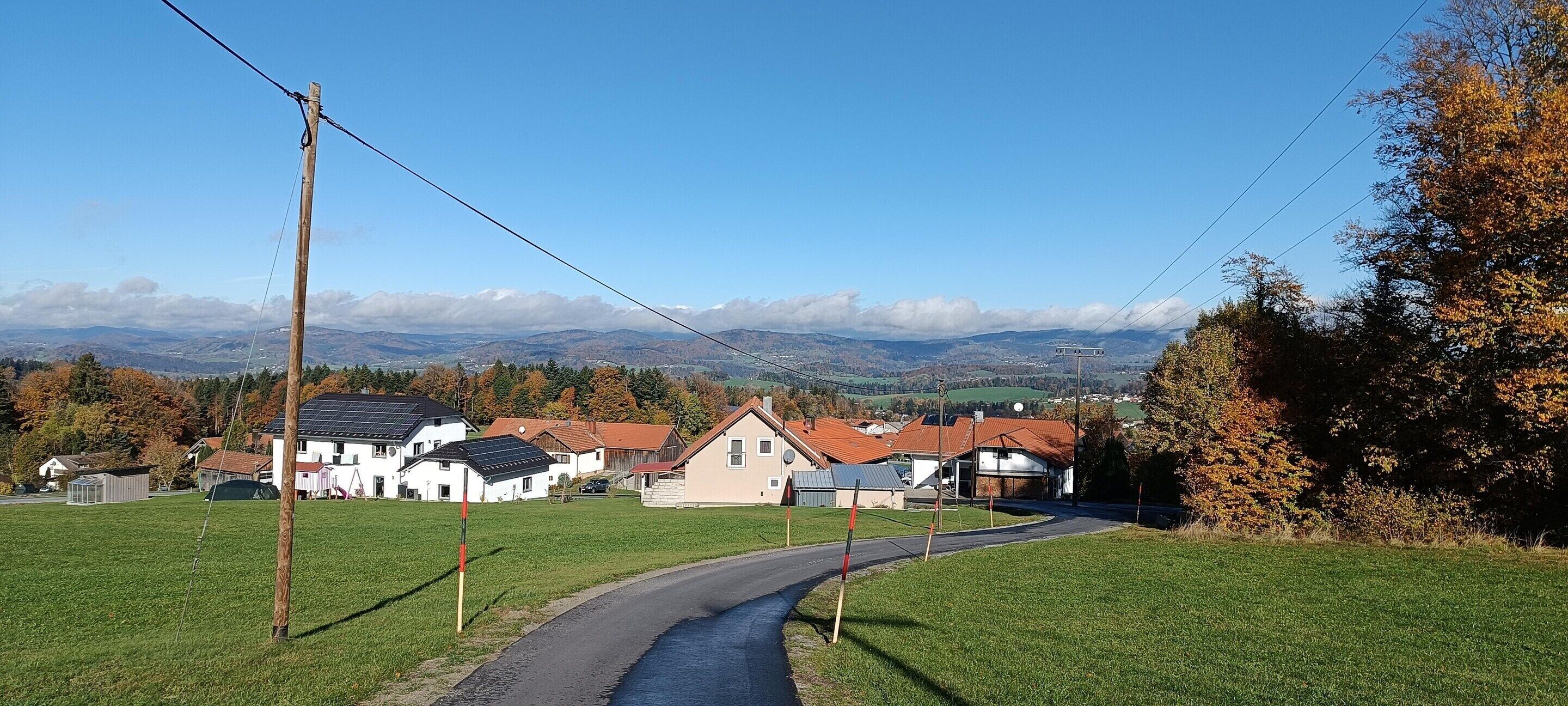 A rural road curving through a green landscape with houses and a view of distant mountains.