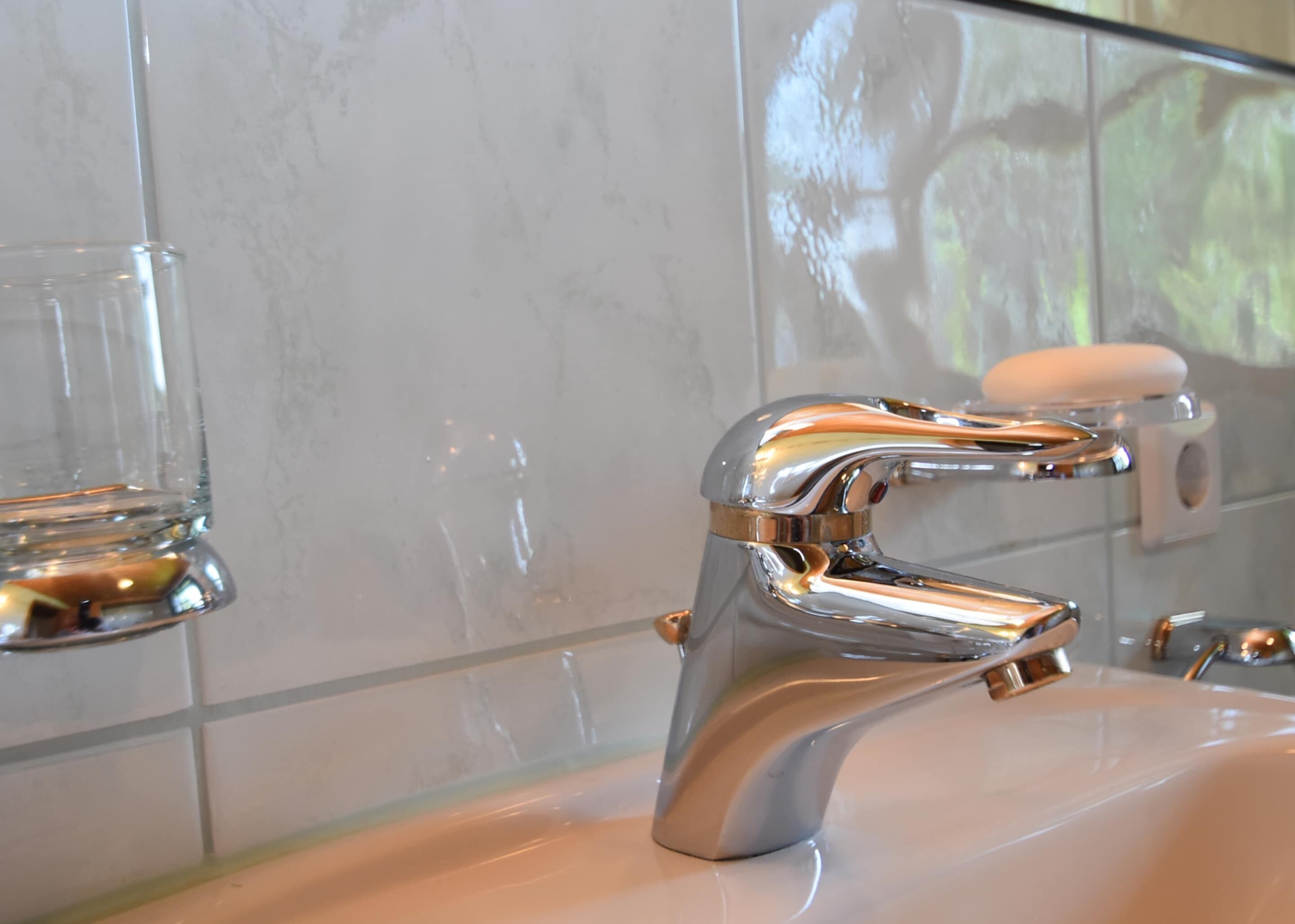 Un bagno con un rubinetto cromato, un portasapone in vetro e uno schienale in marmo.