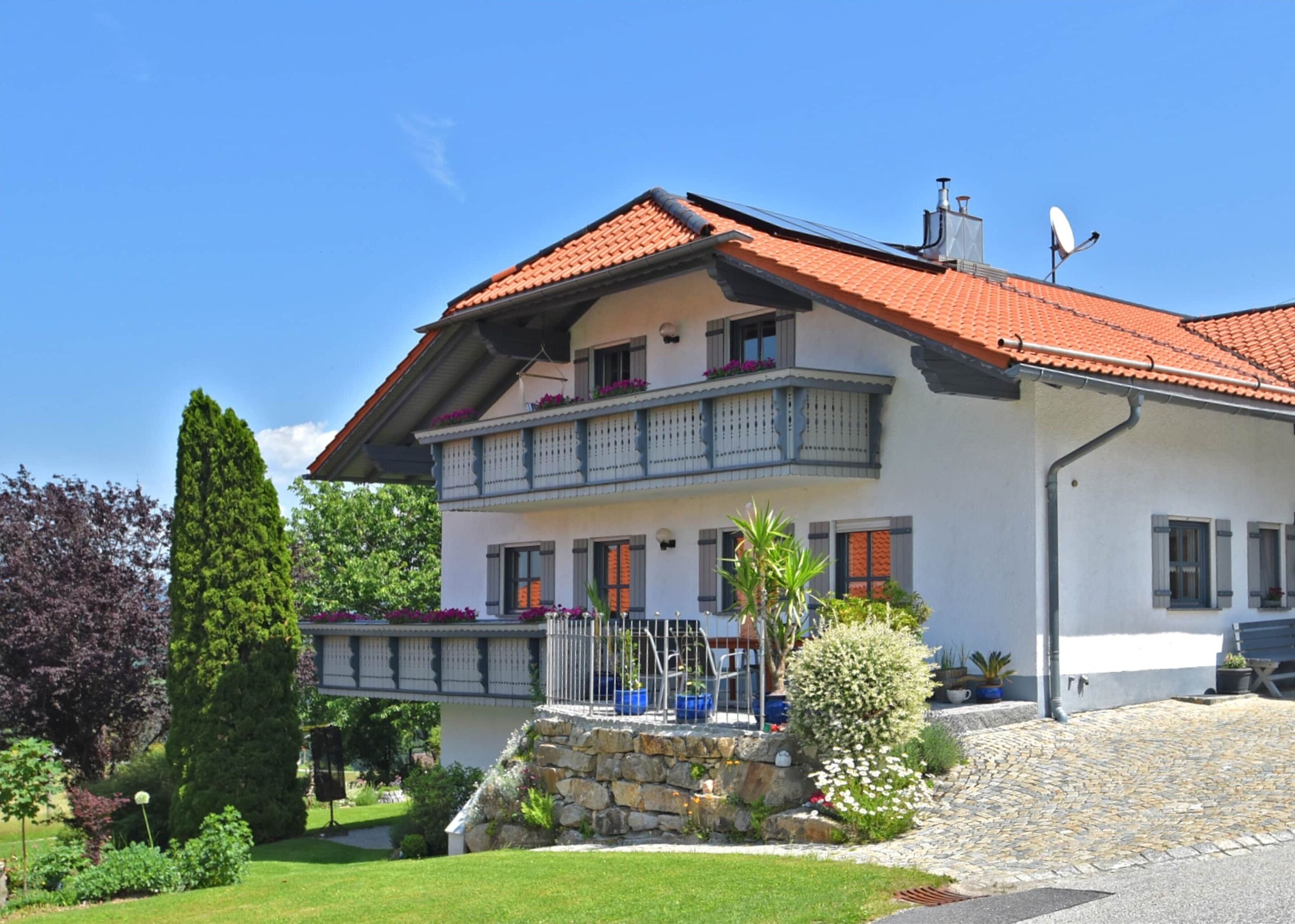 Una casa a due piani con tetto in tegole rosse, un balcone con ringhiere e una scala in pietra che conduce all'ingresso.