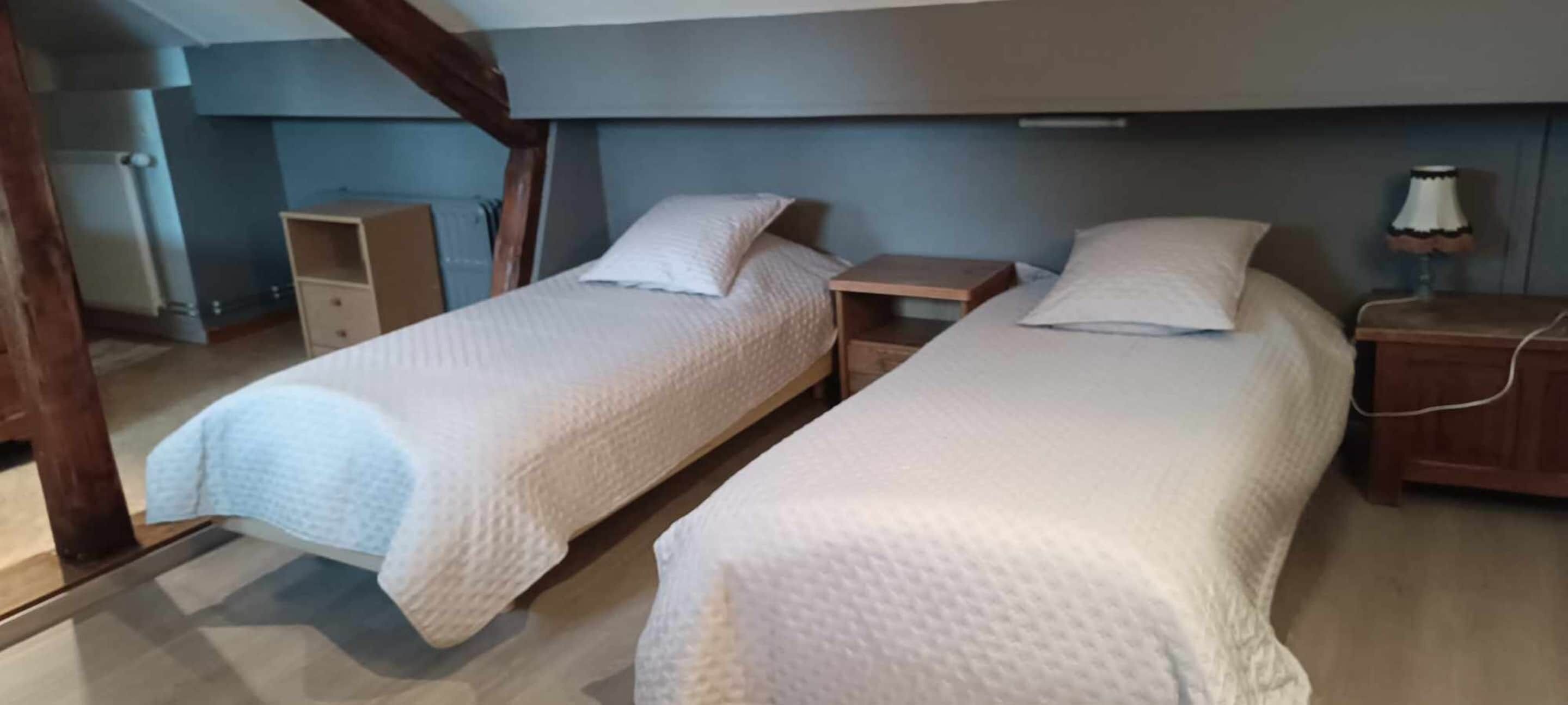 A room with two single beds, wooden nightstands, and a small desk.