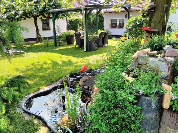 Stroll through the serene garden, surrounded by lush greenery and a tranquil pond, with a patio area perfect for relaxation.