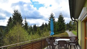 A patio with a table and chairs, a blue umbrella, and a view of a forested area. - Mountain Hideaway in Wildenthal (Eibenstock)