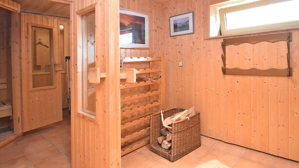 A wooden interior with a wooden door, a wall-mounted shelf, a wicker basket with firewood, and a framed picture on the wall. - Mountain Hideaway in Wildenthal (Eibenstock)
