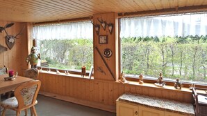 A wooden cabin interior with a dining table, chairs, a bench, and a window with curtains. - Mountain Hideaway in Wildenthal (Eibenstock)