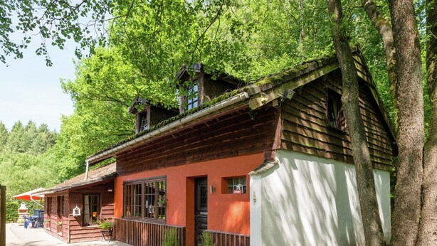 Un bâtiment traditionnel en bois, doté d’une façade rouge, d’un balcon et d’un chemin de gravier menant à un espace aménagé pour s’asseoir.