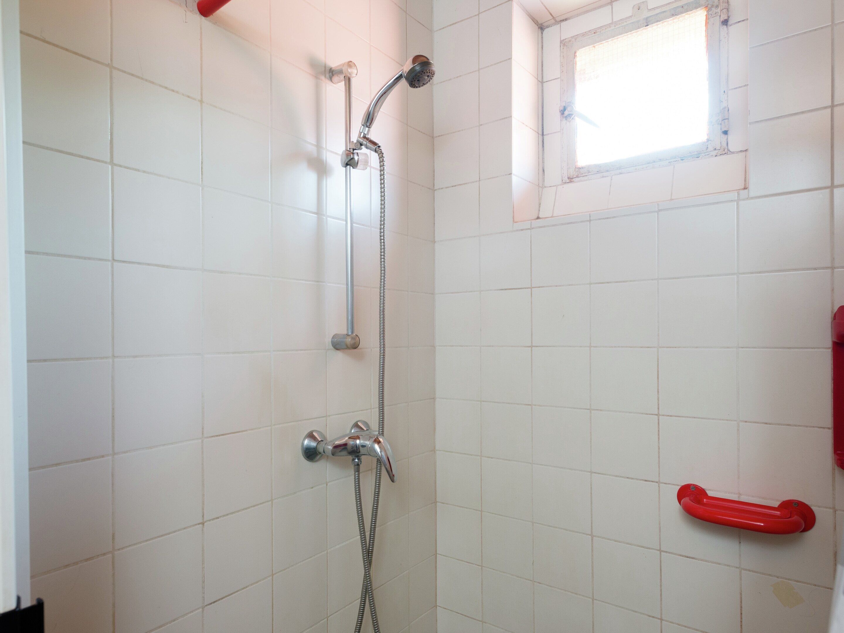 Une douche équipée d’un pommeau de douche à main et d’un robinet fixé au mur.