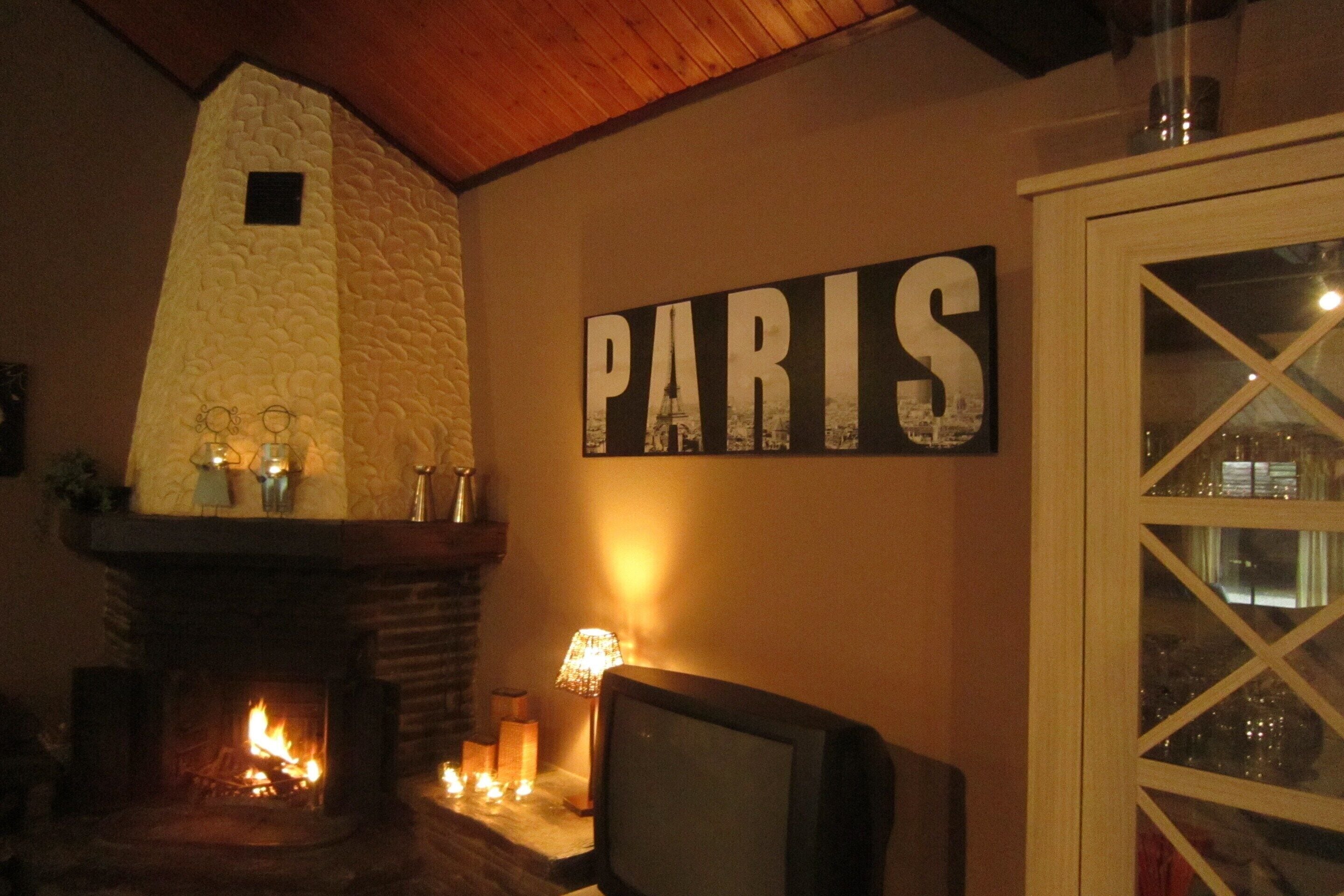 Um quarto aconchegante com lareira de pedra, televisão e um letreiro na parede com a palavra 'PARIS'.