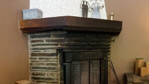 Une cheminée en pierre avec un manteau en bois, un présentoir en métal et un panier en osier.