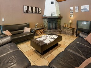 Un salon avec une cheminée en pierre, un canapé, un téléviseur et un panneau mural sur lequel on peut lire « PARIS ».