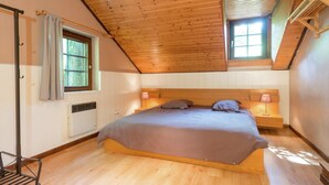 Une chambre avec un plafond en pente, un lit, une fenêtre et un radiateur.