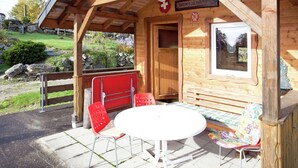 A wooden chalet with a covered patio, a table, and two red chairs.