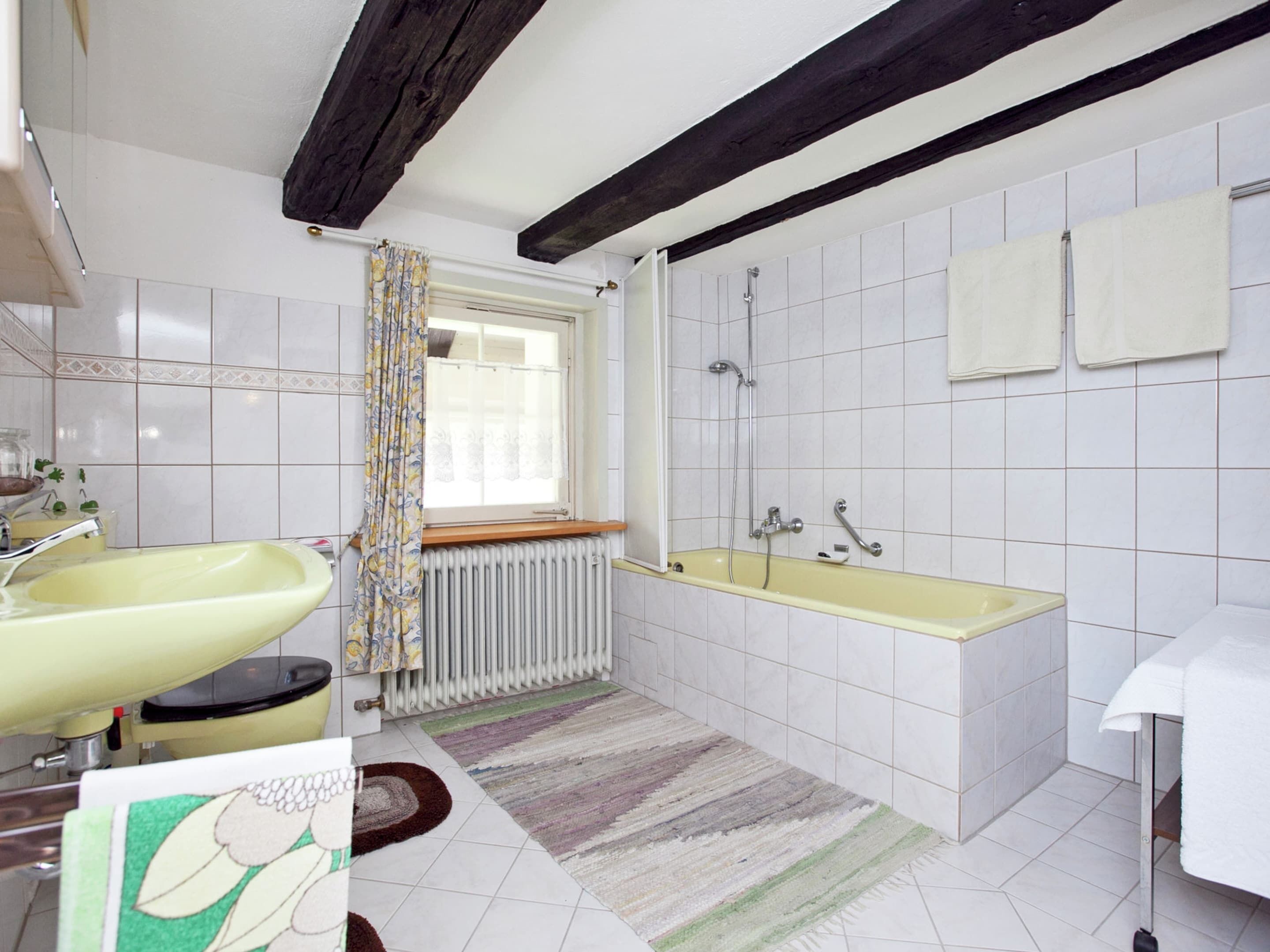A bathroom with a yellow sink, a bathtub, a window with a curtain, and a radiator.