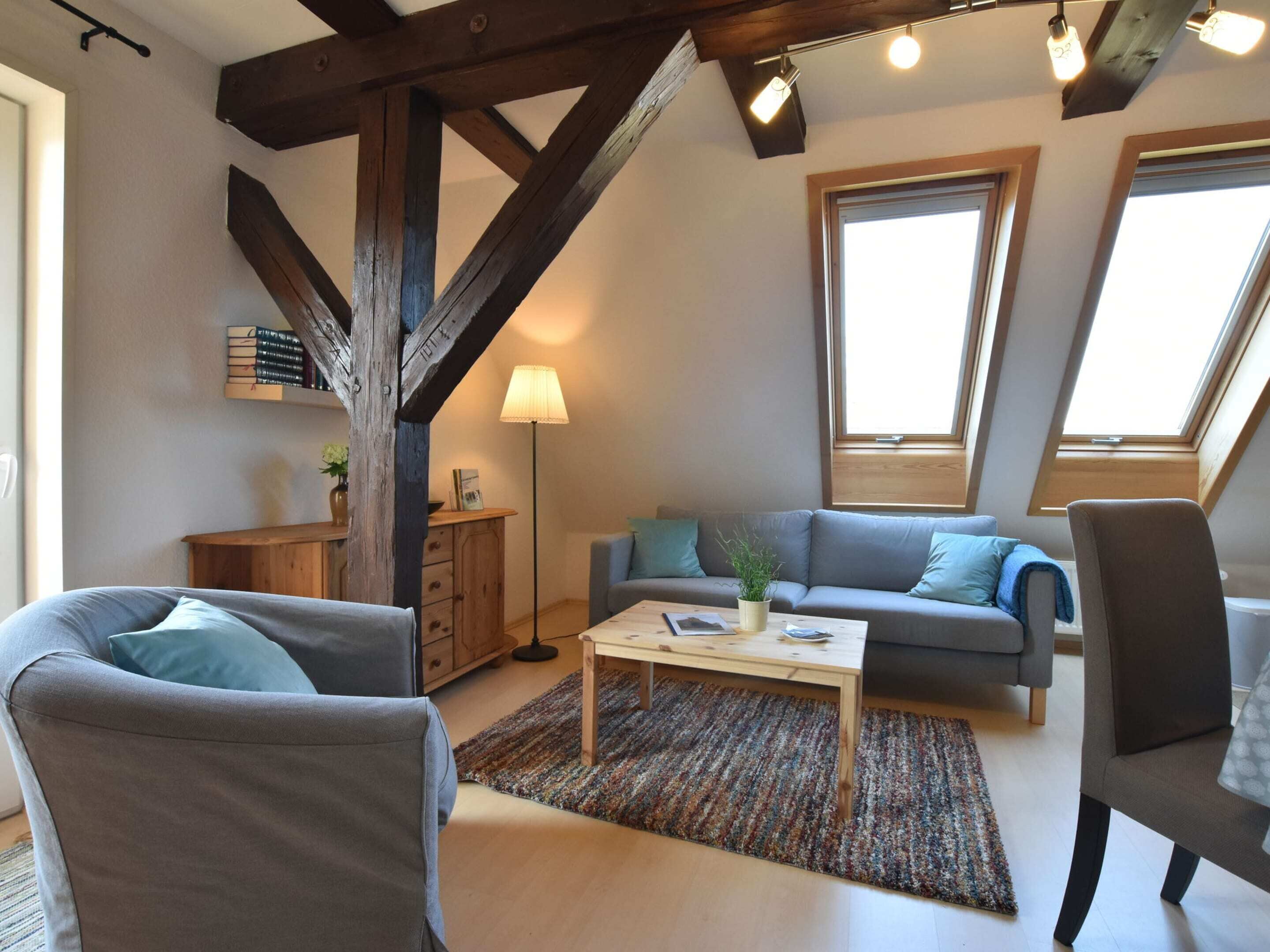 A cozy living room with a wooden ceiling, a grey sofa, a coffee table, and a large window.