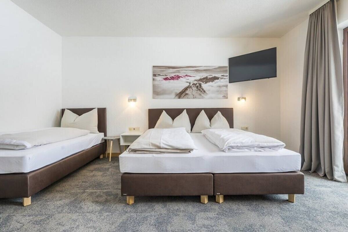 A hotel room with two beds, a flat-screen TV, a painting of a mountain, and a window with curtains.