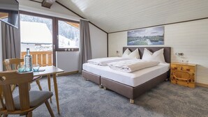 Un dormitorio con cama, una silla de madera, una mesa y un ventanal con vistas a un paisaje nevado.