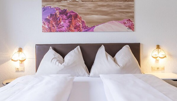 A hotel room with a large bed, two bedside lamps, and a painting of a mountainous landscape on the wall. - Stadlhof Flachau (Flachau)