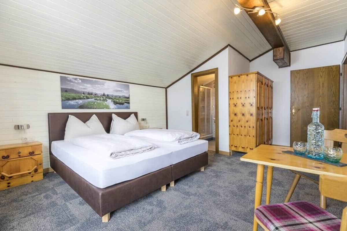 A bedroom with a bed, wooden wardrobe, and a table with decorative items.