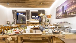 Un bufé de desayuno con una variedad de alimentos y bebidas, una mesa de madera y una vista panorámica de montañas al fondo.