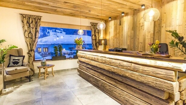 Un mostrador de recepción de madera con un amplio ventanal, un sofá y una pequeña mesa con un jarrón de flores.