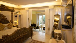 Quarto com uma cama grande, área de estar com mesa e cadeiras, e um espelho na parede.