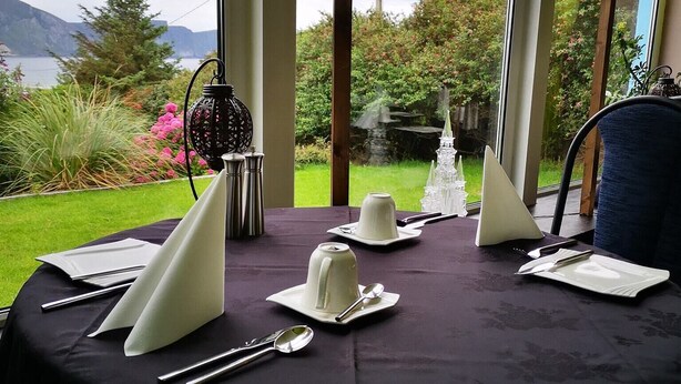 Mesa posta para refeição, com vista para um jardim e montanhas.