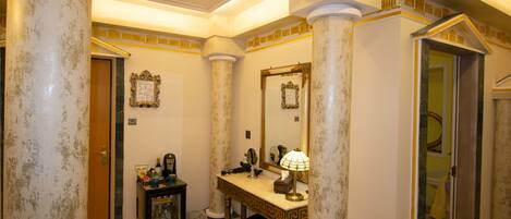 A bathroom with marble columns, a vanity with a mirror, a sink, and a shower area.