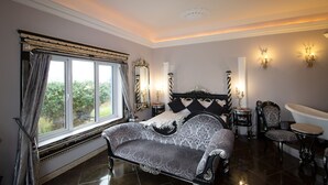 Quarto com cama grande, chaise longue, banheira e janela com cortinas.