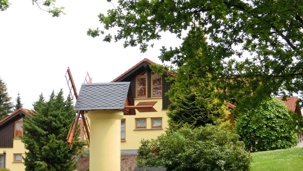 Ein gelbes Gebäude mit Windmühle, umgeben von viel Grün und Bäumen.