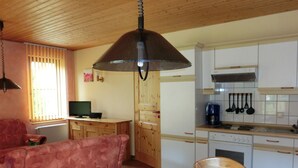 Ein gemütlicher Wohnbereich mit einer Couch, einem Esstisch mit kariertem Tischläufer und einer Küche mit weißen Schränken und Holzarbeitsplatten.
