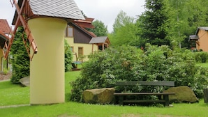 Ein traditioneller Windmüller, eine hölzerne Bank und eine Steinmauer inmitten eines üppigen Gartens.