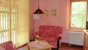 Ein gemütliches Wohnzimmer mit einem rosa Sofa, einem Holztisch mit Blumenvase und einem Fenster mit Jalousien.