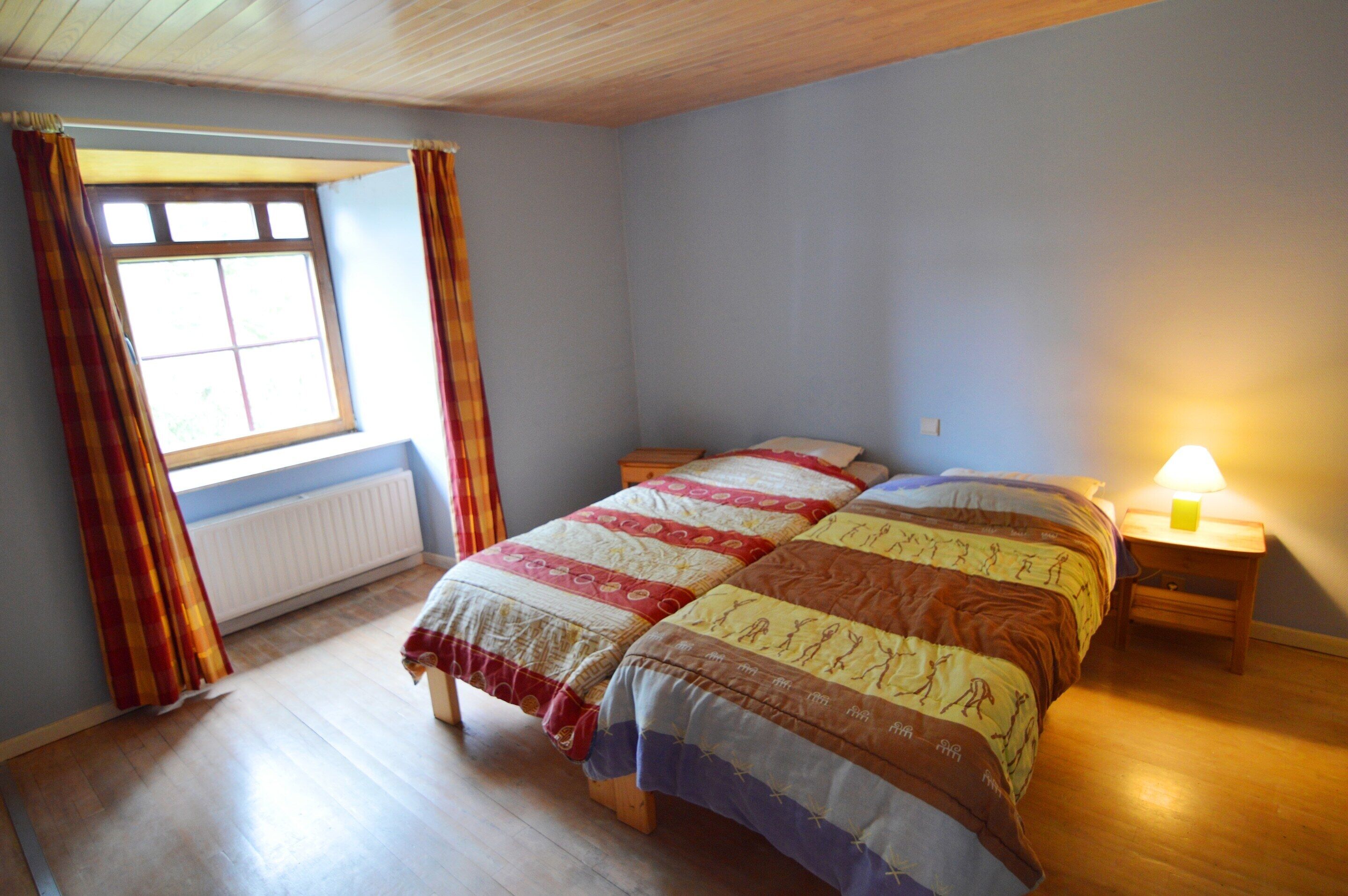 Et soveværelse med en stor seng, et vindue med gardiner, et sengebord med en lampe og en radiator.