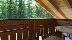 Una terraza de madera con una mesa y sillas, con vistas a un área boscosa.