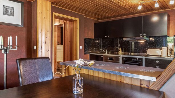A modern kitchen with dark cabinets, a wooden ceiling, and a dining area with a table and chairs. - Apartment in Wittenbeck Near Baltic Sea (Wittenbeck)