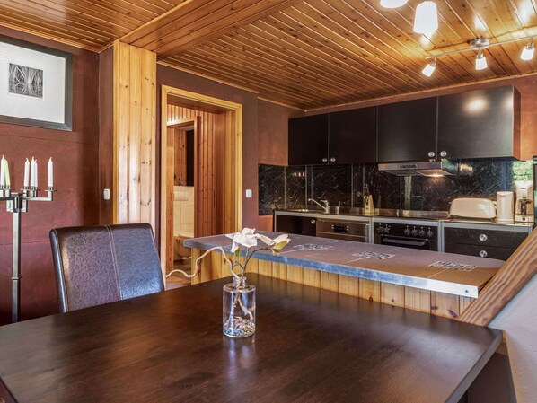 A modern kitchen with dark cabinets, a wooden ceiling, and a dining area with a table and chairs. - Apartment in Wittenbeck Near Baltic Sea (Wittenbeck)