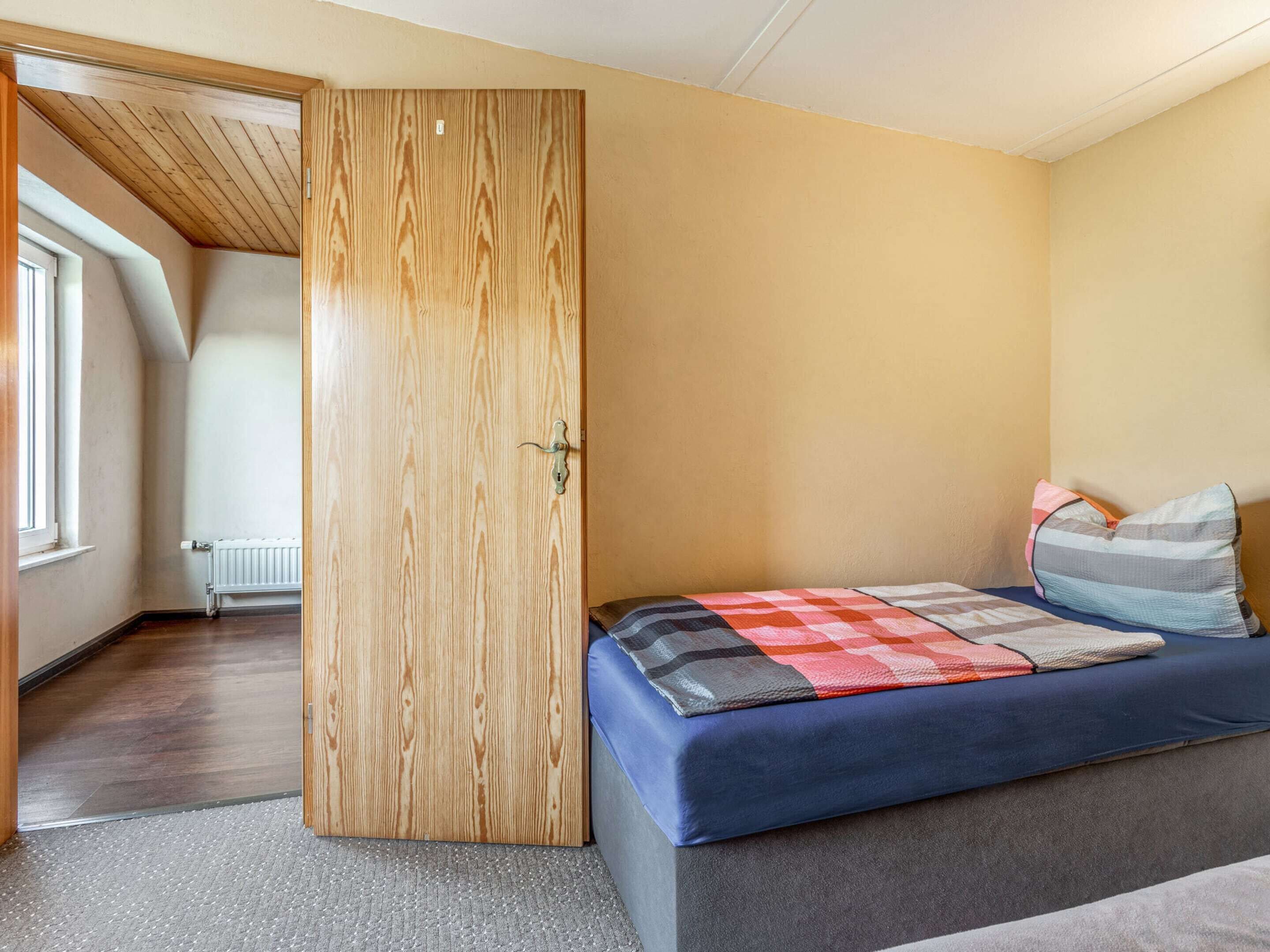 A bedroom with a wooden wardrobe, a bed with a colorful quilt, and a window.
