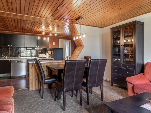 A modern kitchen with dark cabinets, a wooden ceiling, and a dining area with leather chairs and a red sofa. - Apartment in Wittenbeck Near Baltic Sea (Wittenbeck)