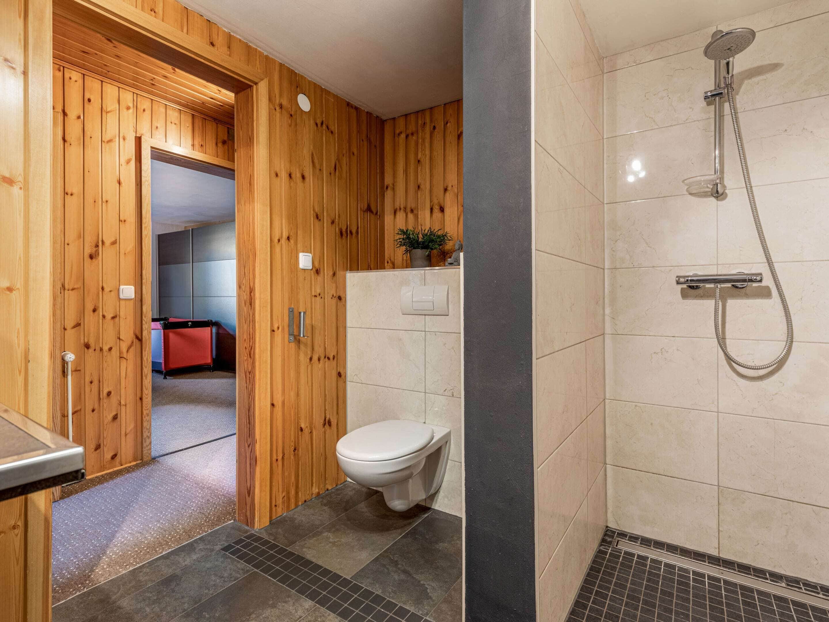 A wooden-paneled bathroom with a shower, a toilet, and a visible red object in the background.