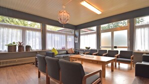 A spacious room with a wooden table, several chairs, a sofa, and large windows with curtains.