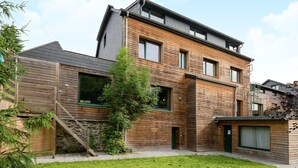 A modern two-story house with a wooden facade, large windows, and a small attached garage.