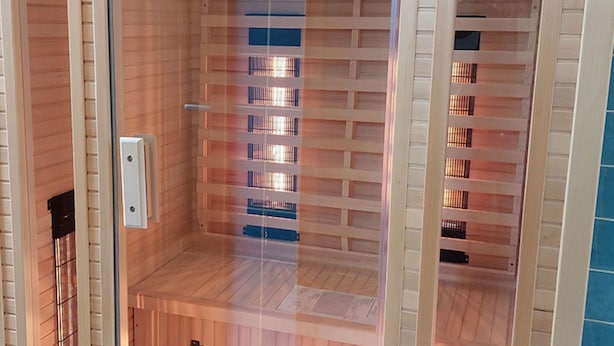 A sauna with a wooden interior and a glass door, featuring a metal rack for towels and a control panel. - Holiday Home With Sauna in the Eifel National Park (Schleiden)